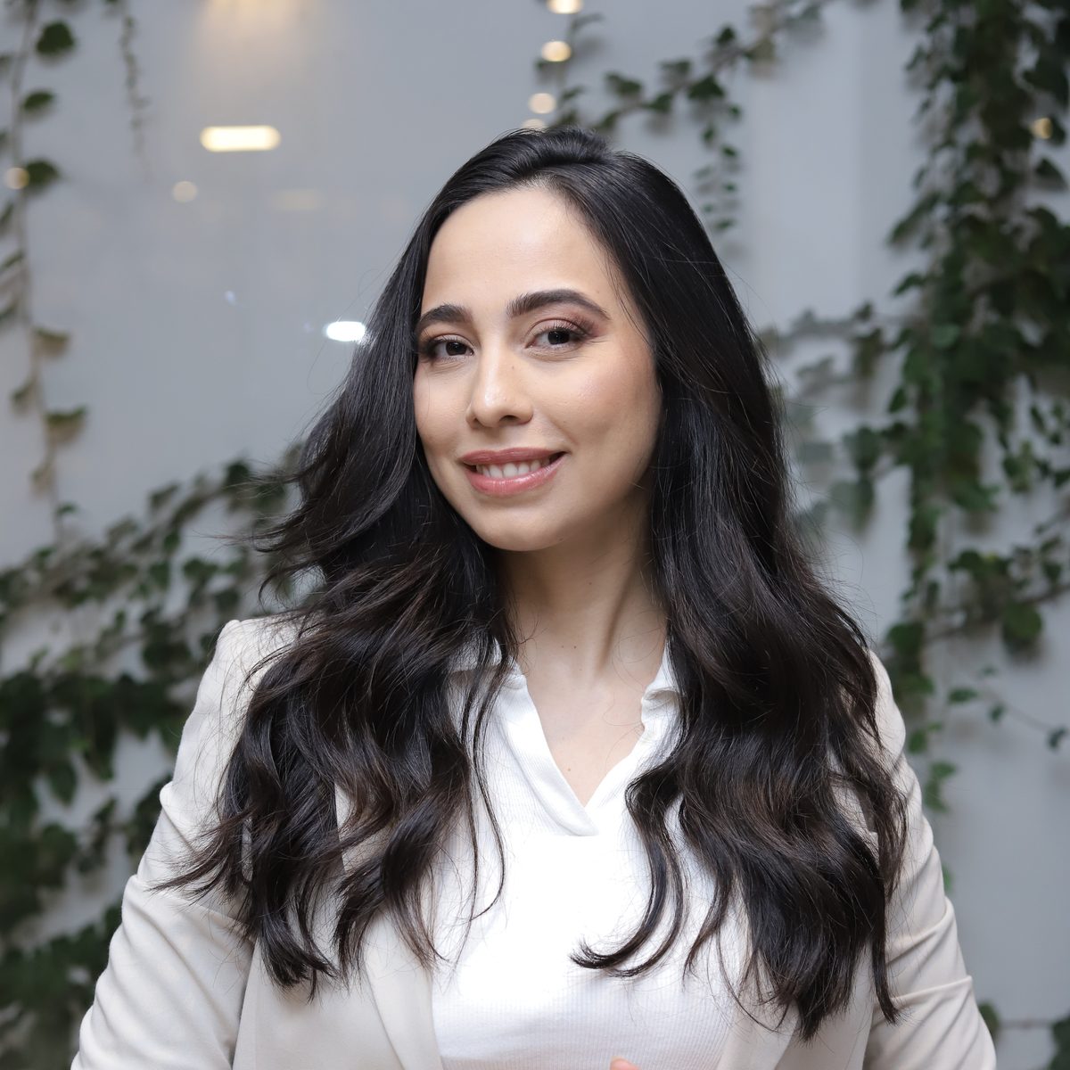 Retrato da Dra. Stephanie Mansan sorrindo, com uma parede de plantas ao fundo